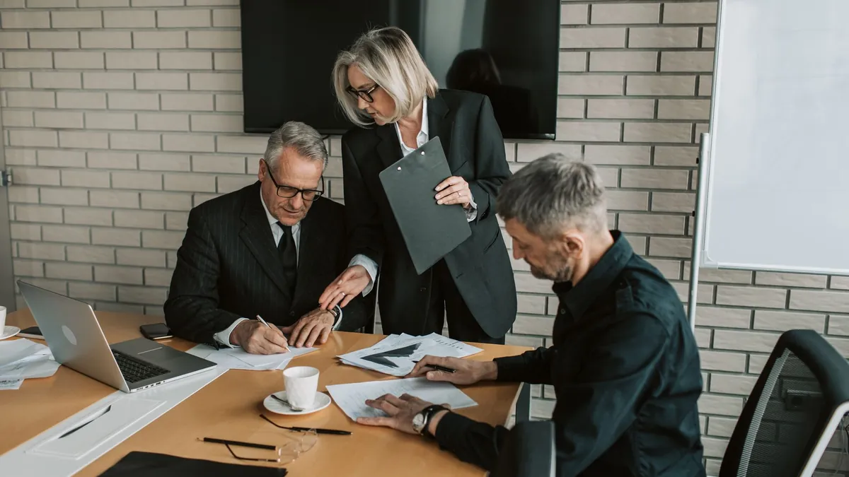 Three people at a meeting table reviewing and signing paperwork
